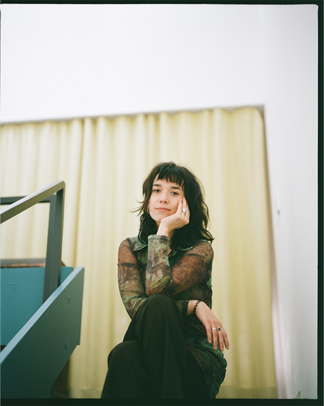 Sarah Miro Fischer sitting on a staircase in front of a pale yellow curtain